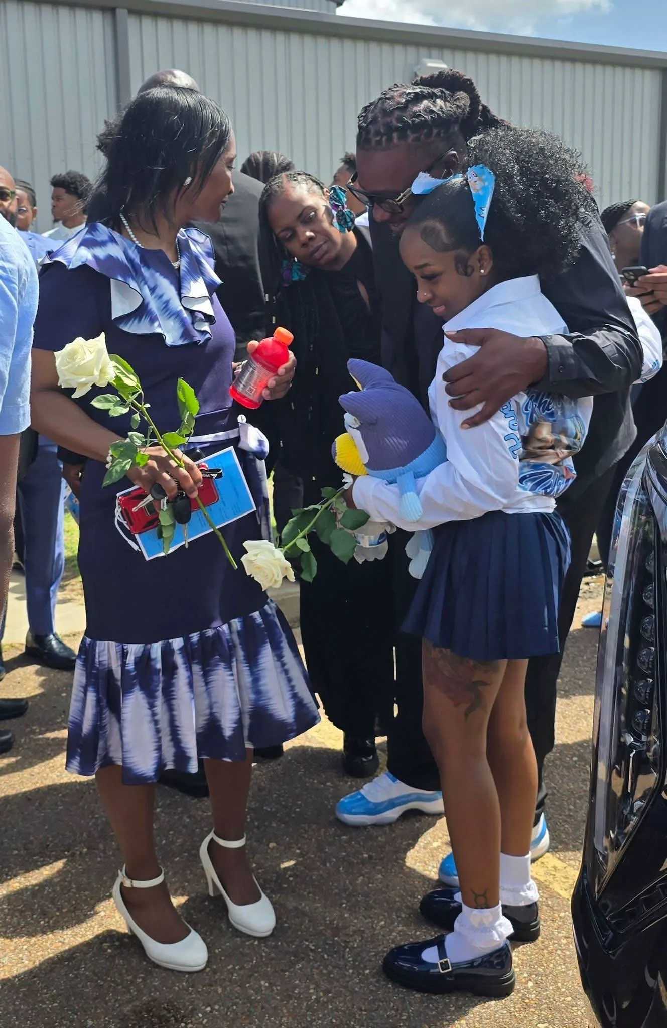 Young loved ones holding flowers and a stuffed toy at a memorial gathering for Kohen